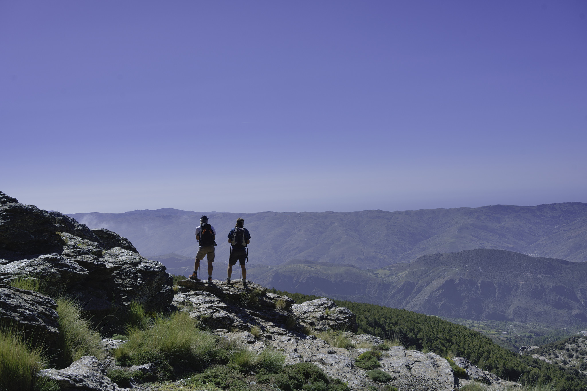 Two hikers look south towards the Sierra de Contraviesa hills and the Mediterranean Sea beyond.