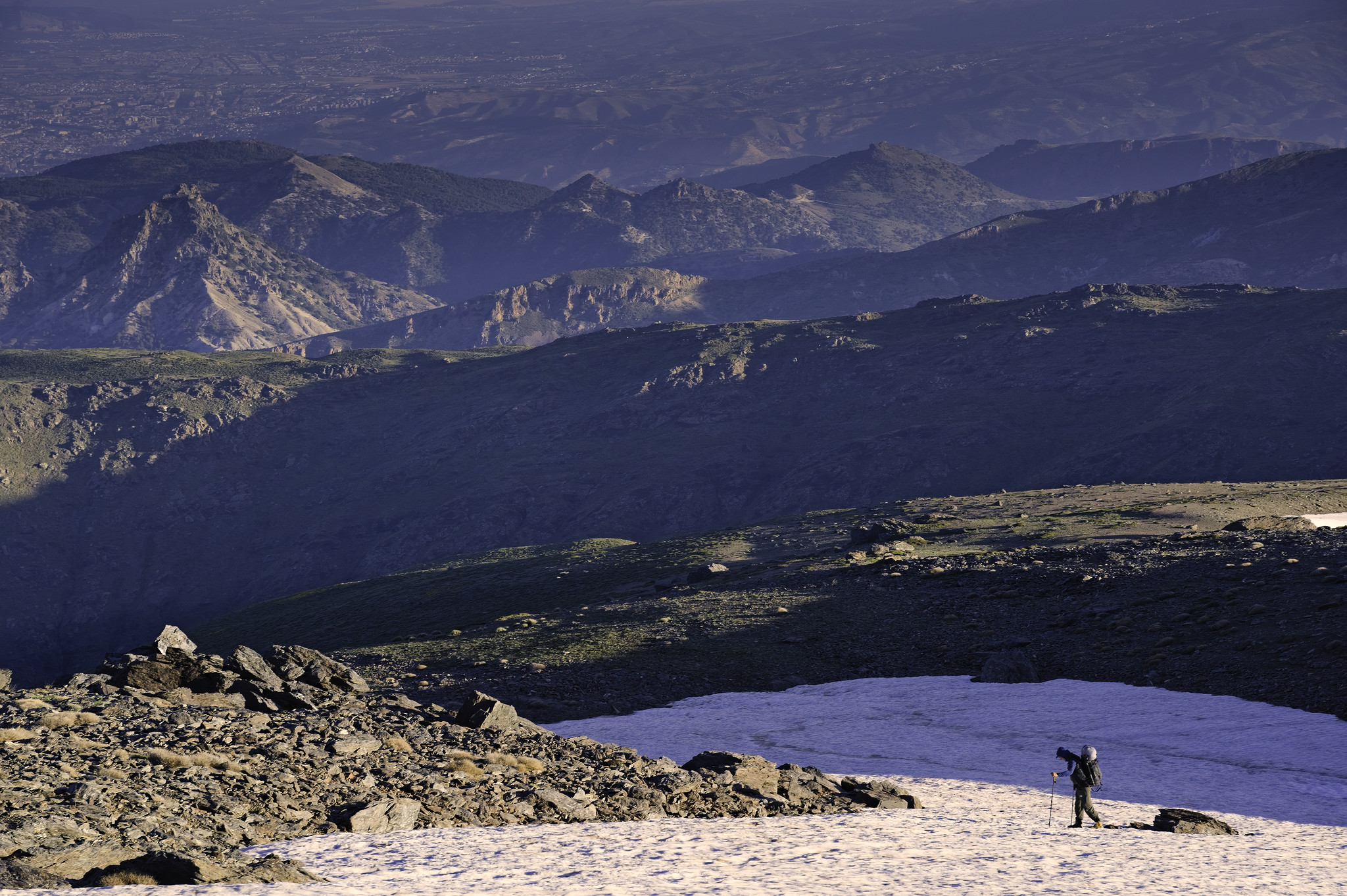 A person is seen crossing a snowfield while lines of light pass across the image. In the distance there are some mountains and a city beyond