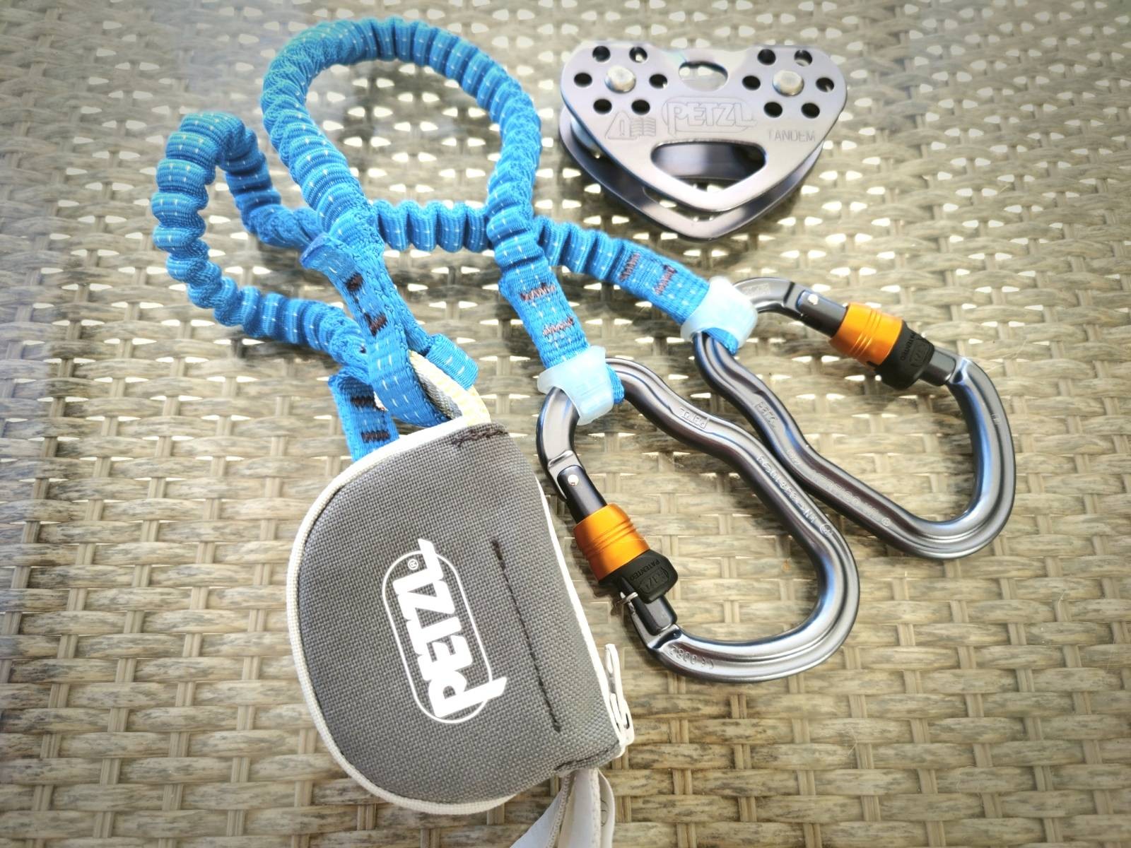 A Petzl Via Ferrata kit consisting of blue lanyards and 2 metal carabiners. At the top is a metal pully.