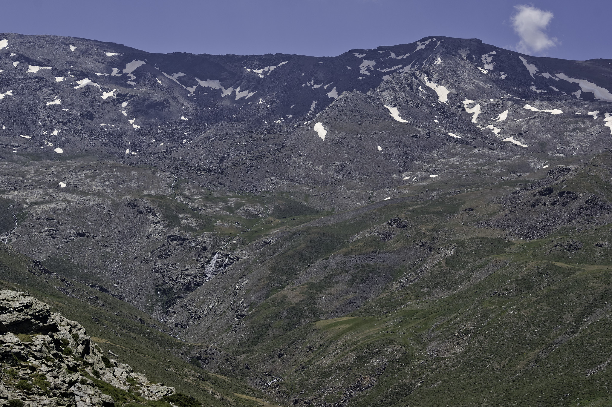 View of a distant mountain range with some snow patches. The main peak is Tozal del Cartujo NW ridge. Some waterfalls (Molinillos) can be seem in the lower left
