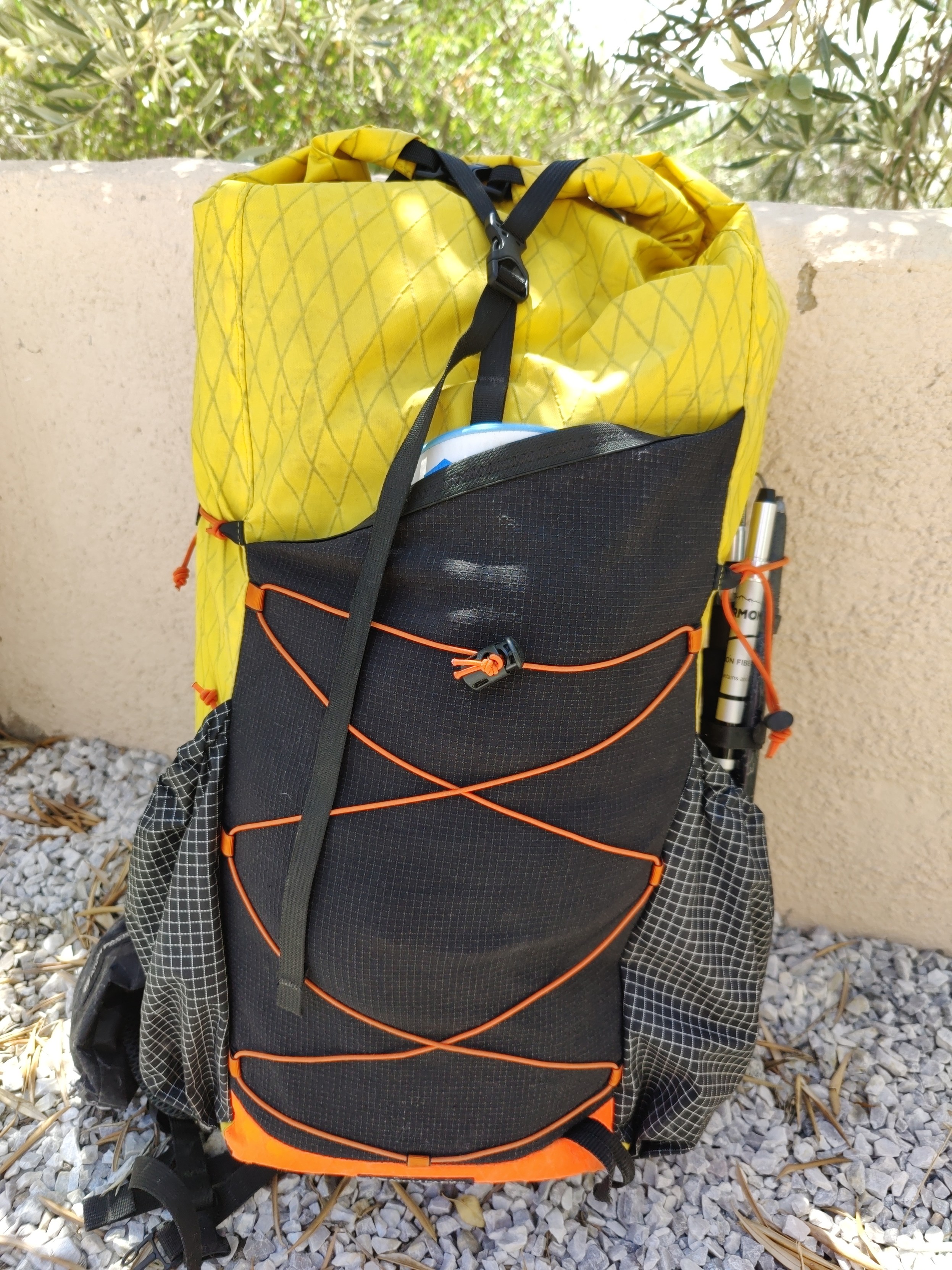A yellow and black 40 litre "Atom Packs" backpack with side pockets, one filled with a trekking pole.