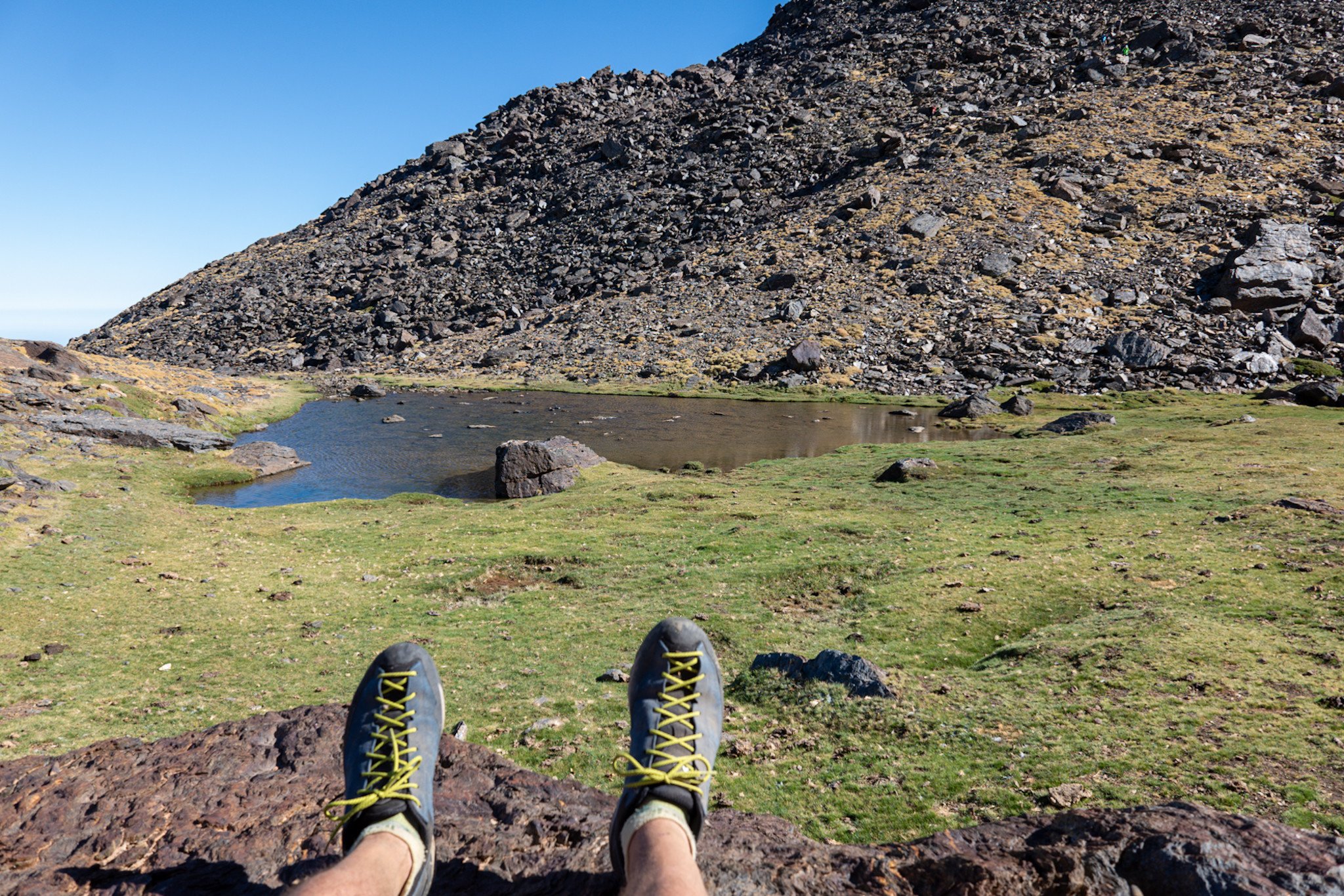 Two feet in some mountain shows are seen in the foreground. Behind lies a small lake with rocky slopes beyond