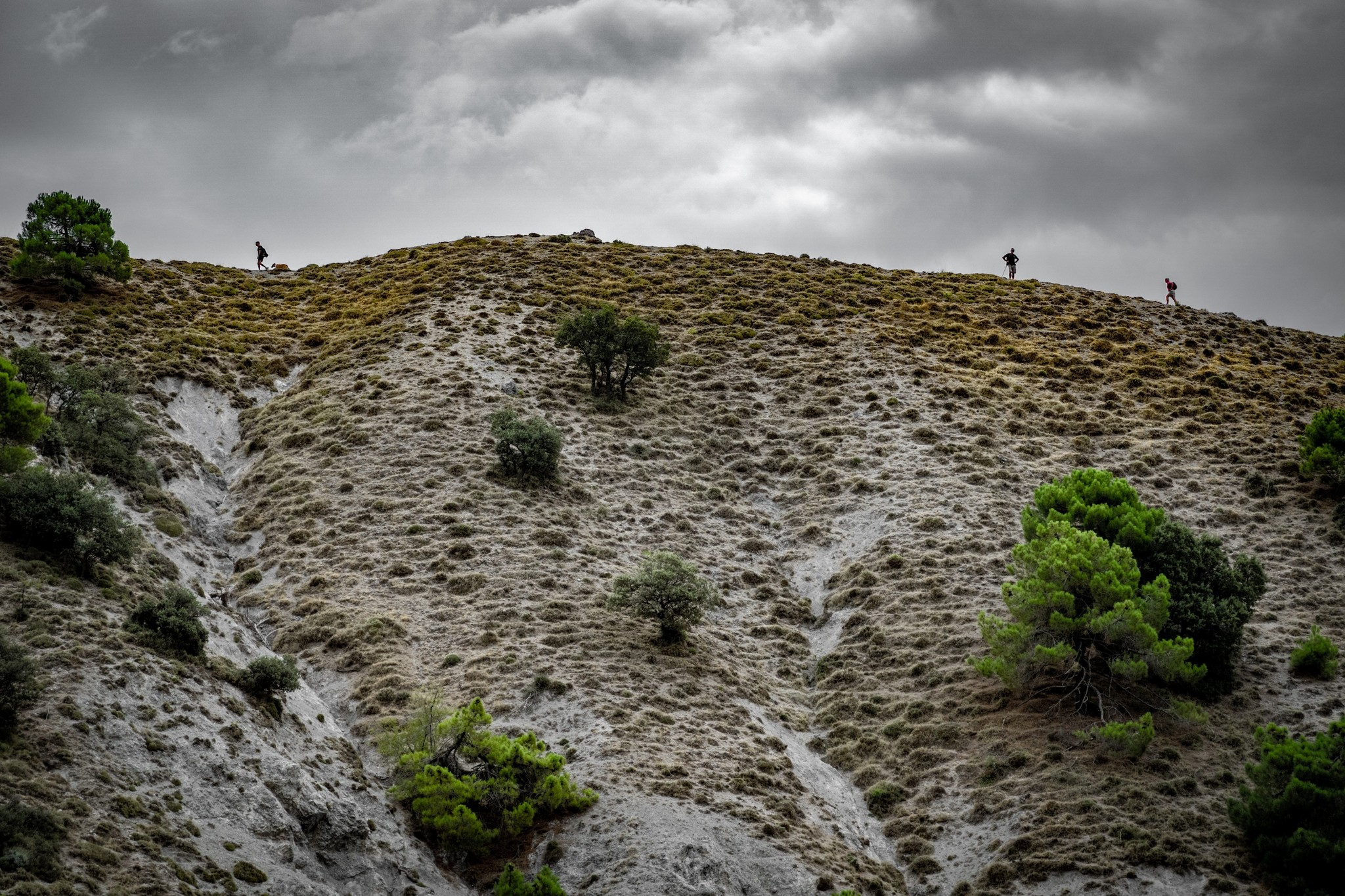 3 hikers silhouetted on the ridge leading to Pico de la Carne. Dark threatening clouds above