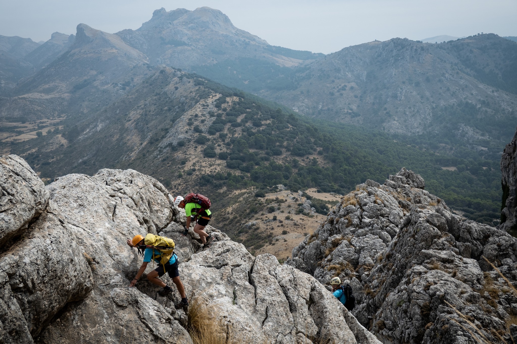 2 people scramble up some easy angled grey rock slabs. Some spectacular mountains in the background