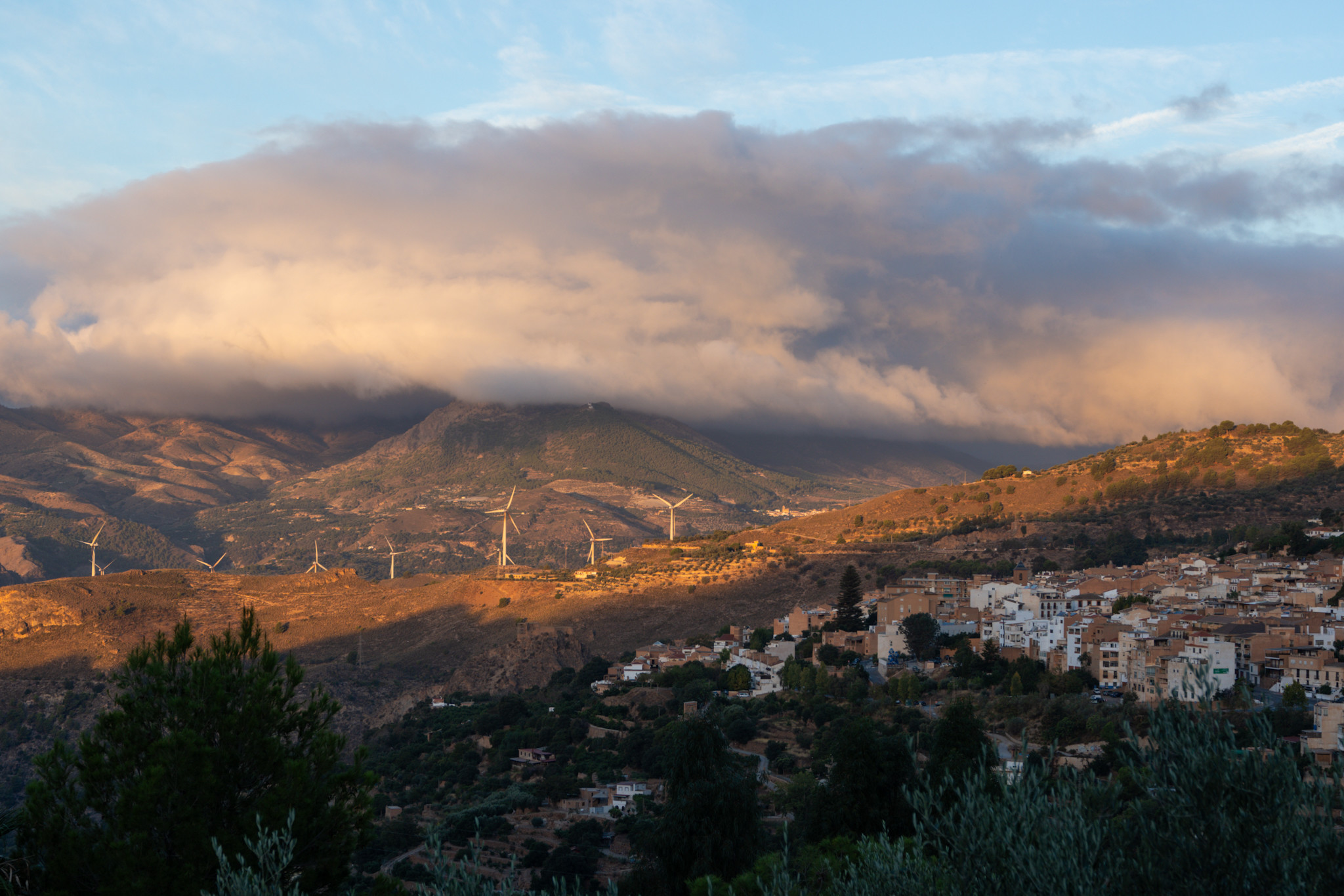 Sun hits the mountain sides above a town. In the background some stunning clouds