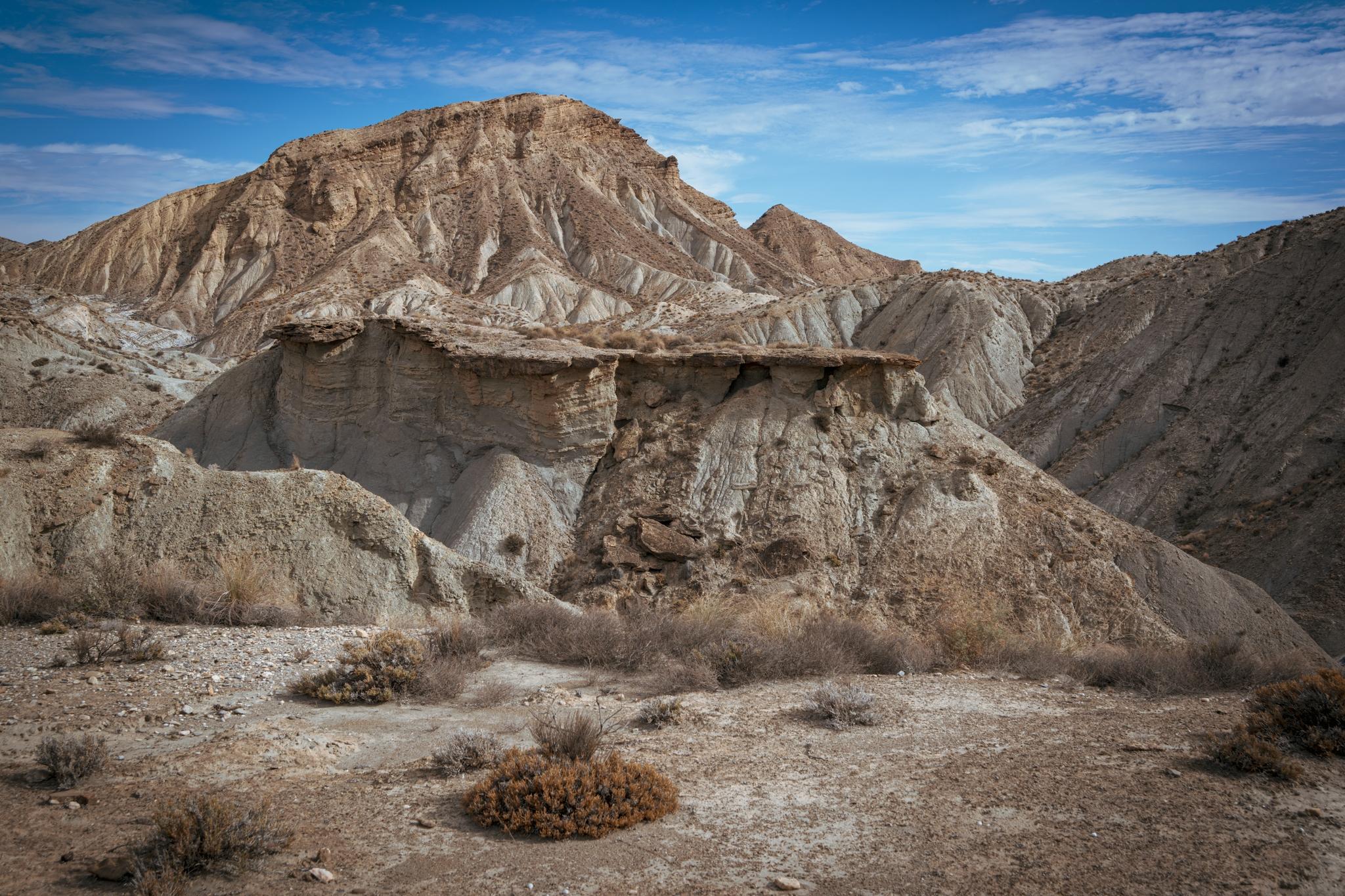 An arid desert badlands scene with a chaotic mass of broken rock and battered, crumbling cliffs