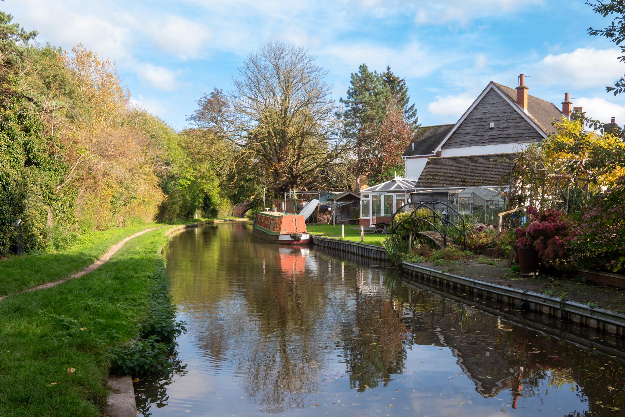 A narrowboat is moored alongside a canal with bright autumn colors