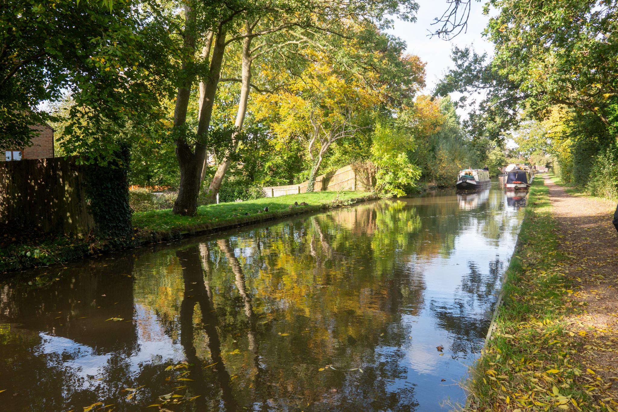 A narrowboat is moored alongside a canal with bright autumn colors