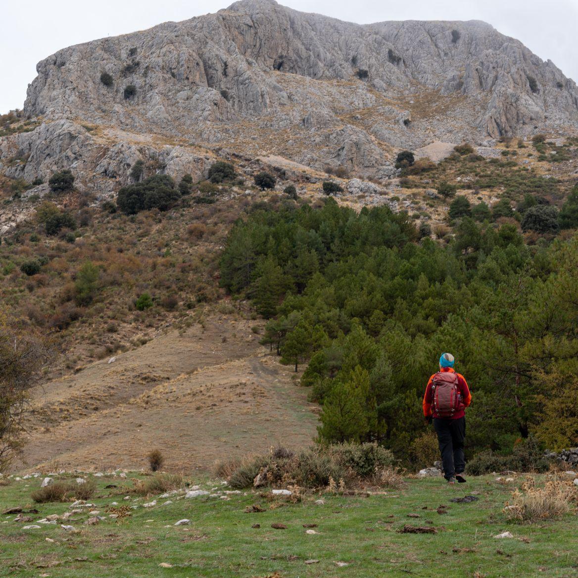 A hiker in red looks up at the west face of Majalijar mountain in the Sierra de Huetor