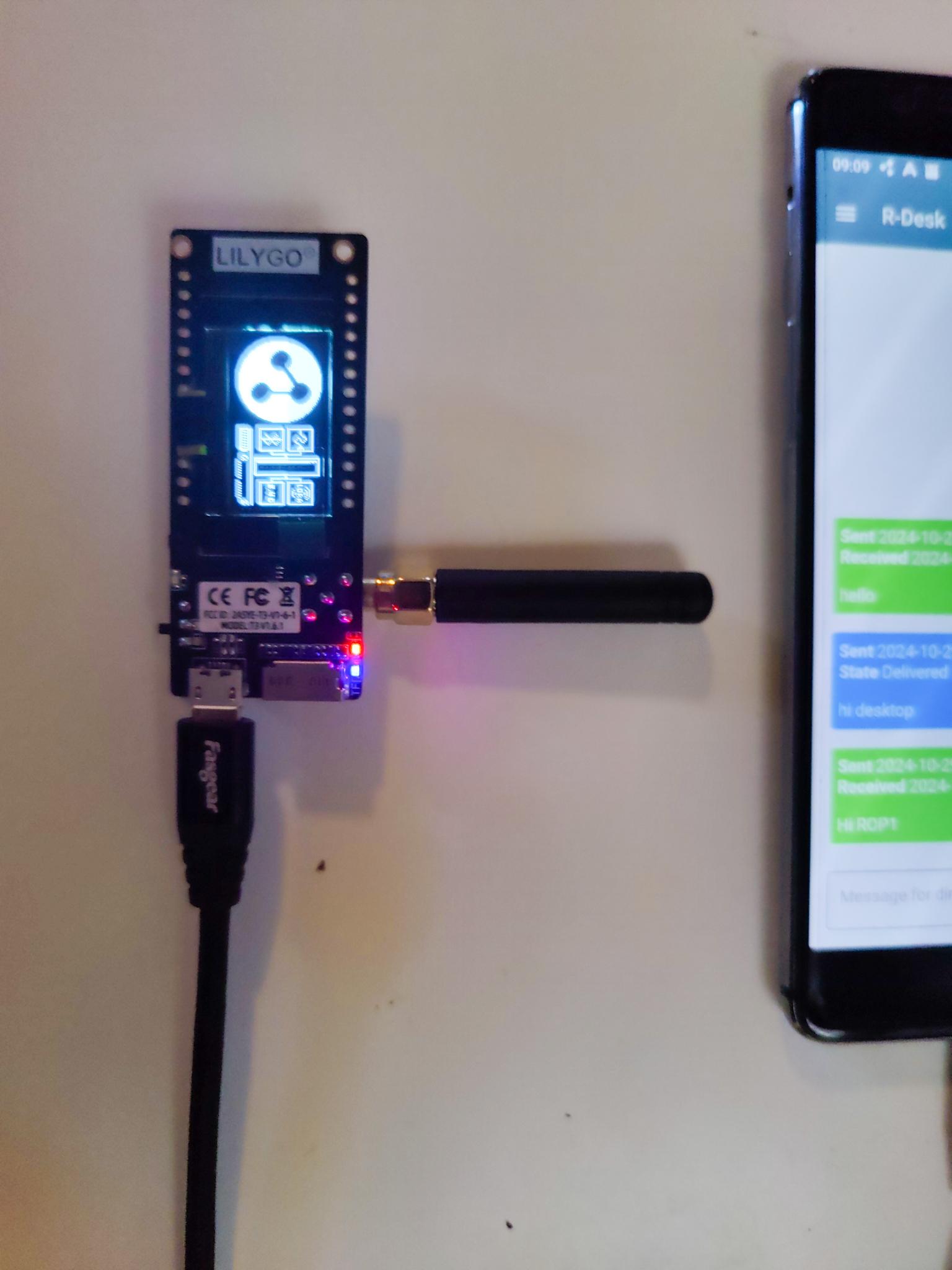 A small computer board with a tiny arial and red light is connected by cable to a phone showing messages.