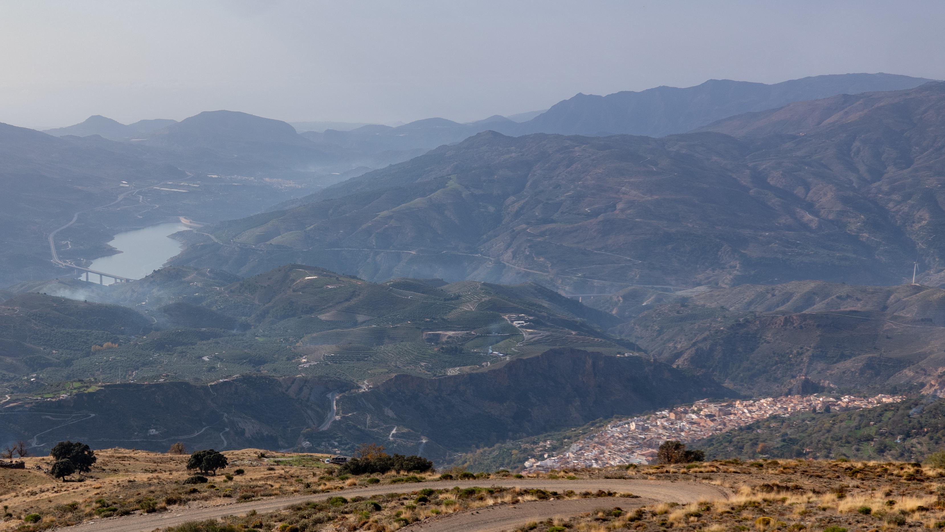 A town is in the bottom right with hills and valleys beyond that lead to a large reservoir.