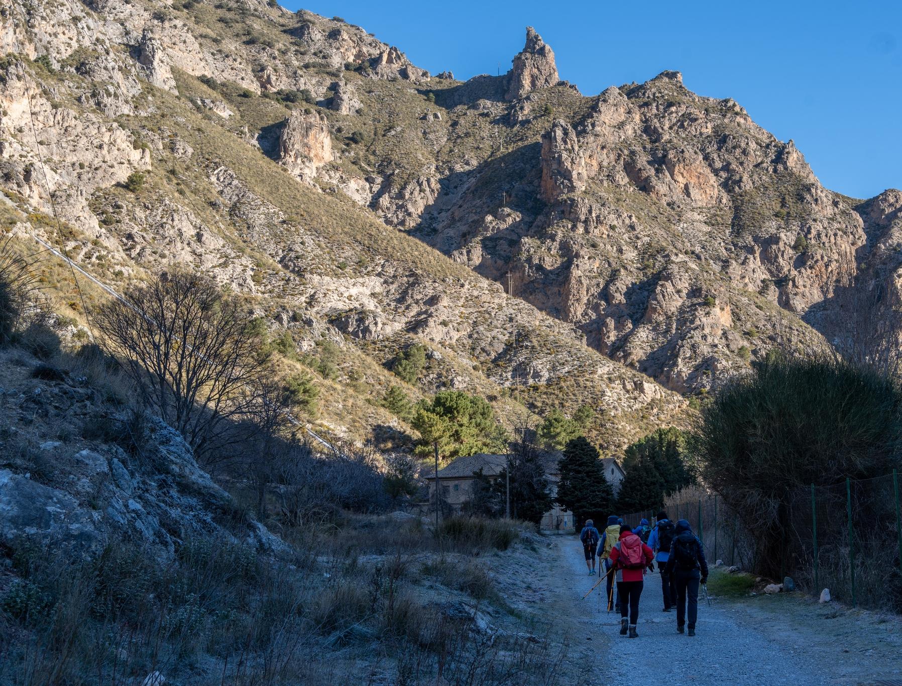 Group of hikers walking in the shade towards a distant mountain peak with sun on it