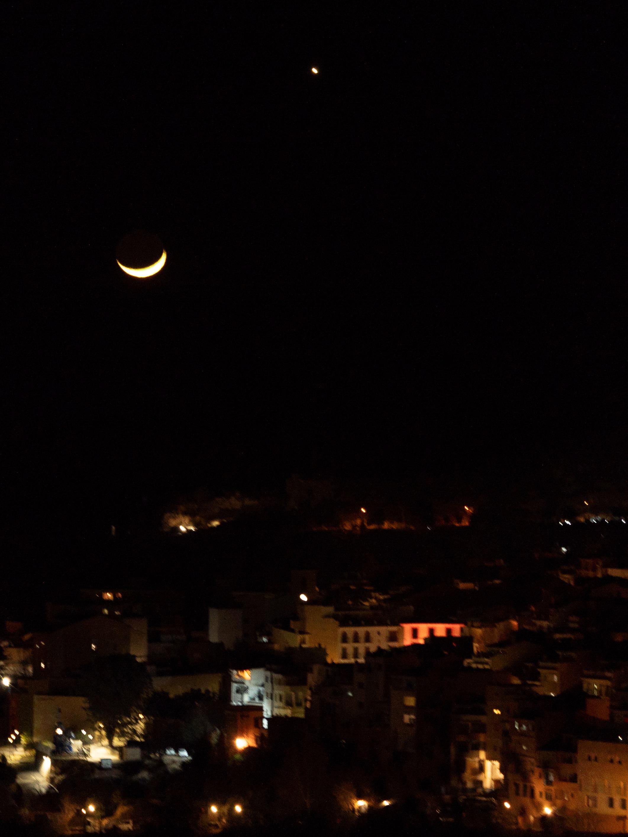 The quarter moon shines above an illuminated spanish town