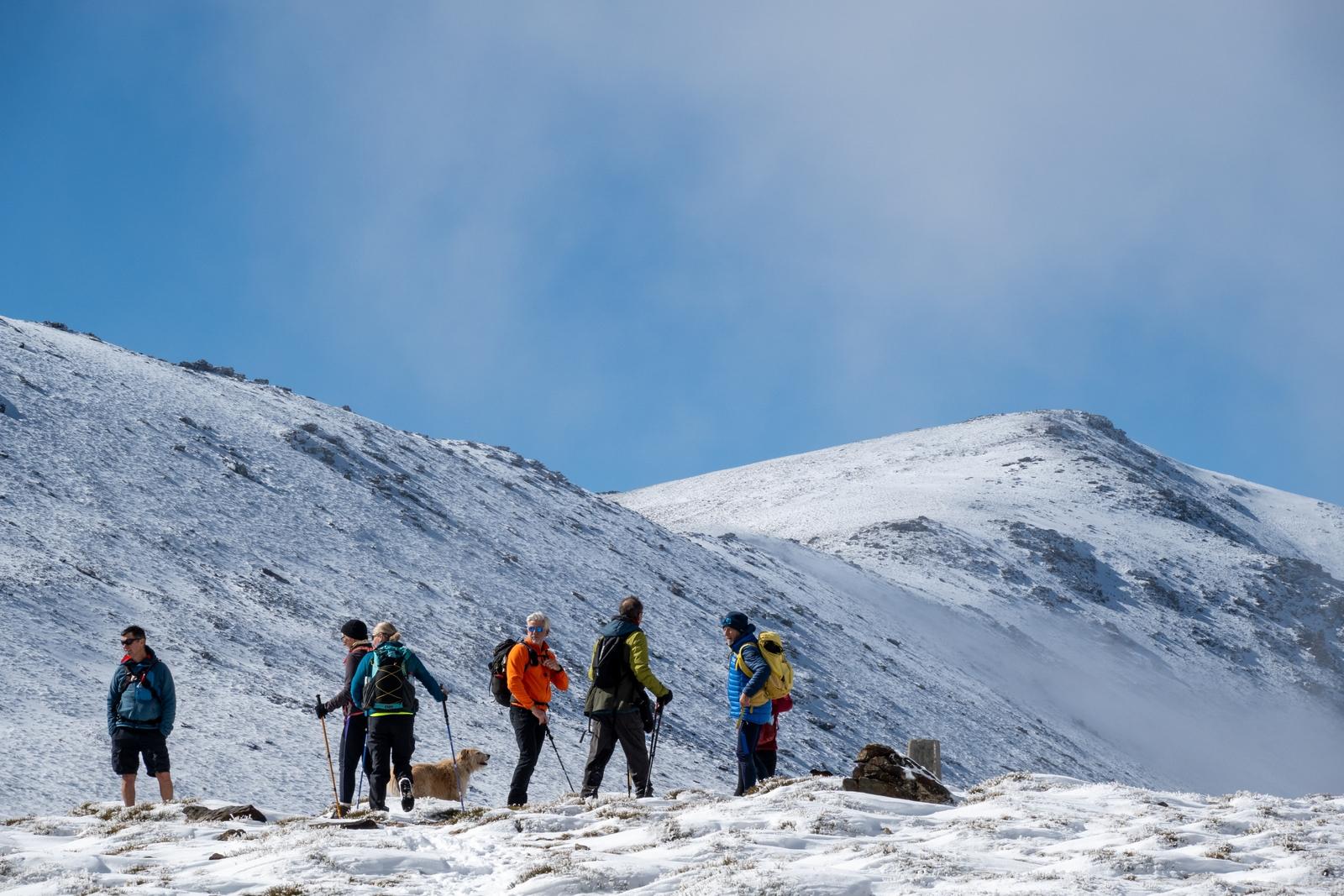 A group of people stand at a pass below some snow clad mountains