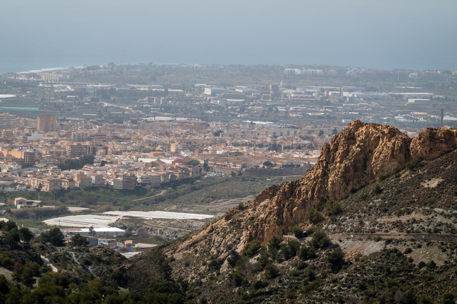 The crag of the Espolon de Cerro Toro in the warm sunshine with the city of Motril behind 
