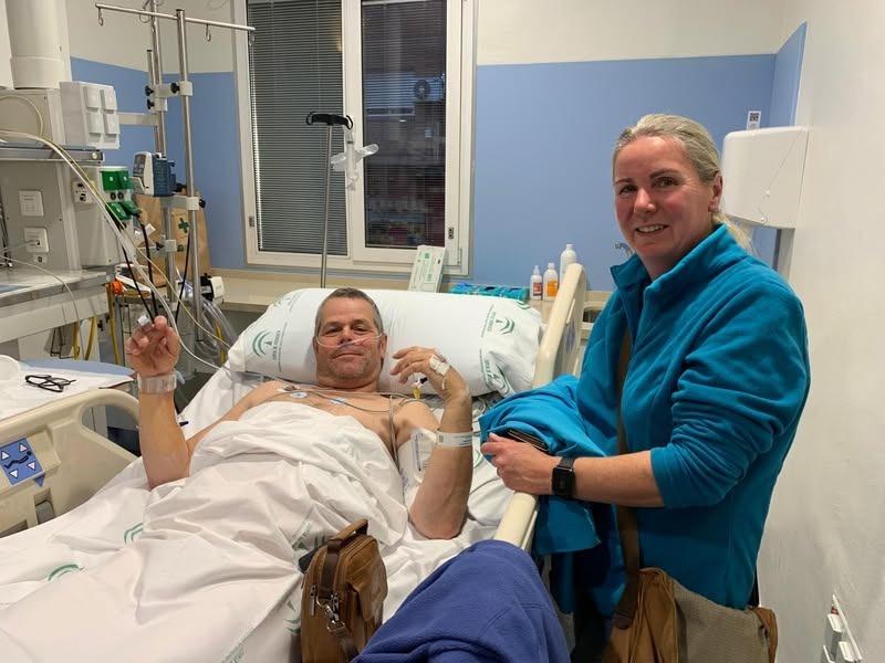 Person in hospital bed (me) all hooked up to various electronics whilst my wife smiles alongside the bed