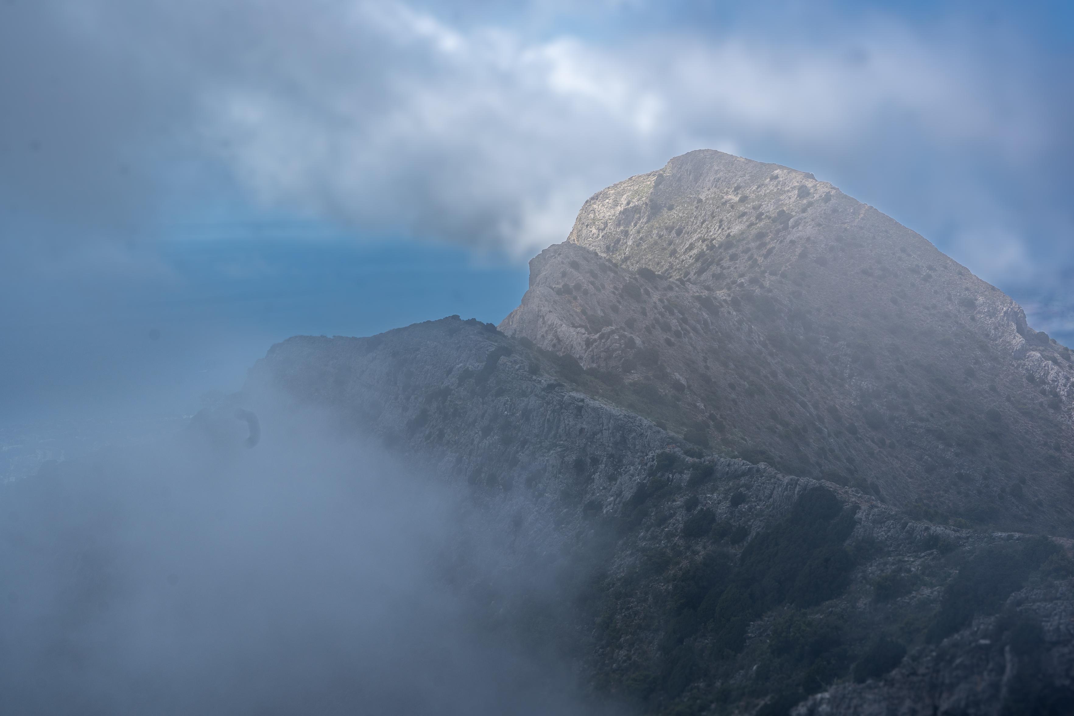 The sun briefly illuminates a mountain summit whilst cloud drifts in and around the ridgelines