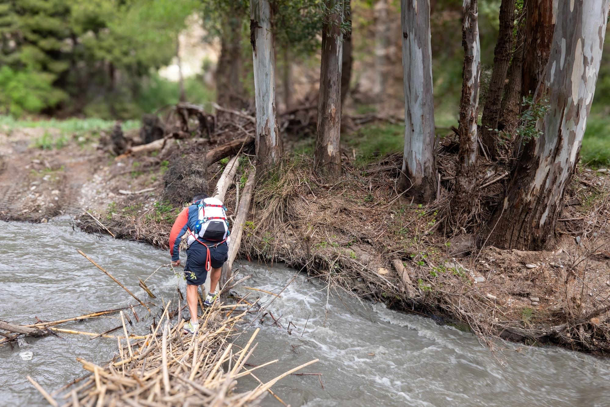 A person trying to cross a fast flowing stream over a dodgy looking fallen tree