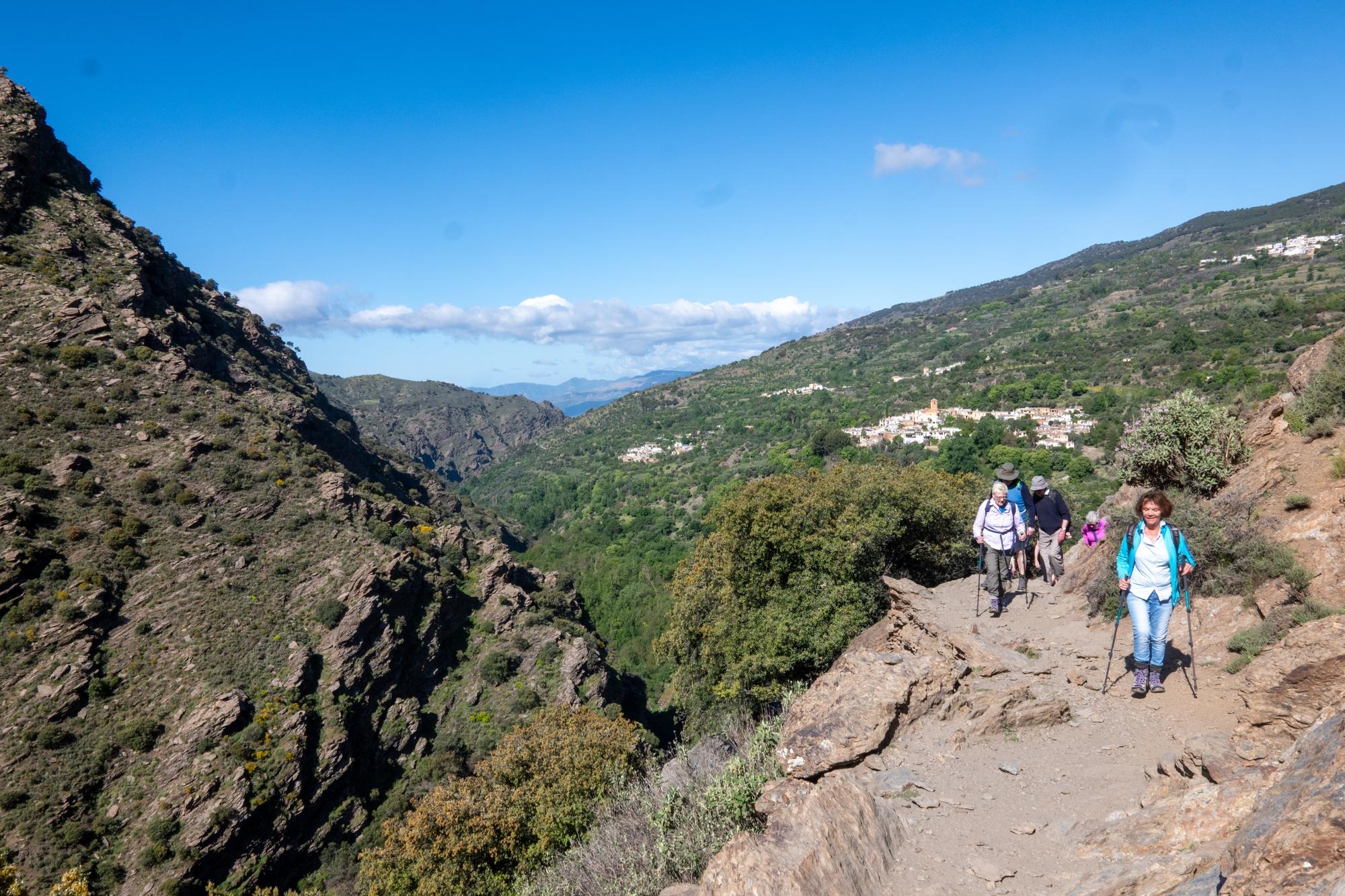Hikers on a high trail above a gorge. Villages of Ferreirola, Mecina and Fondales behind