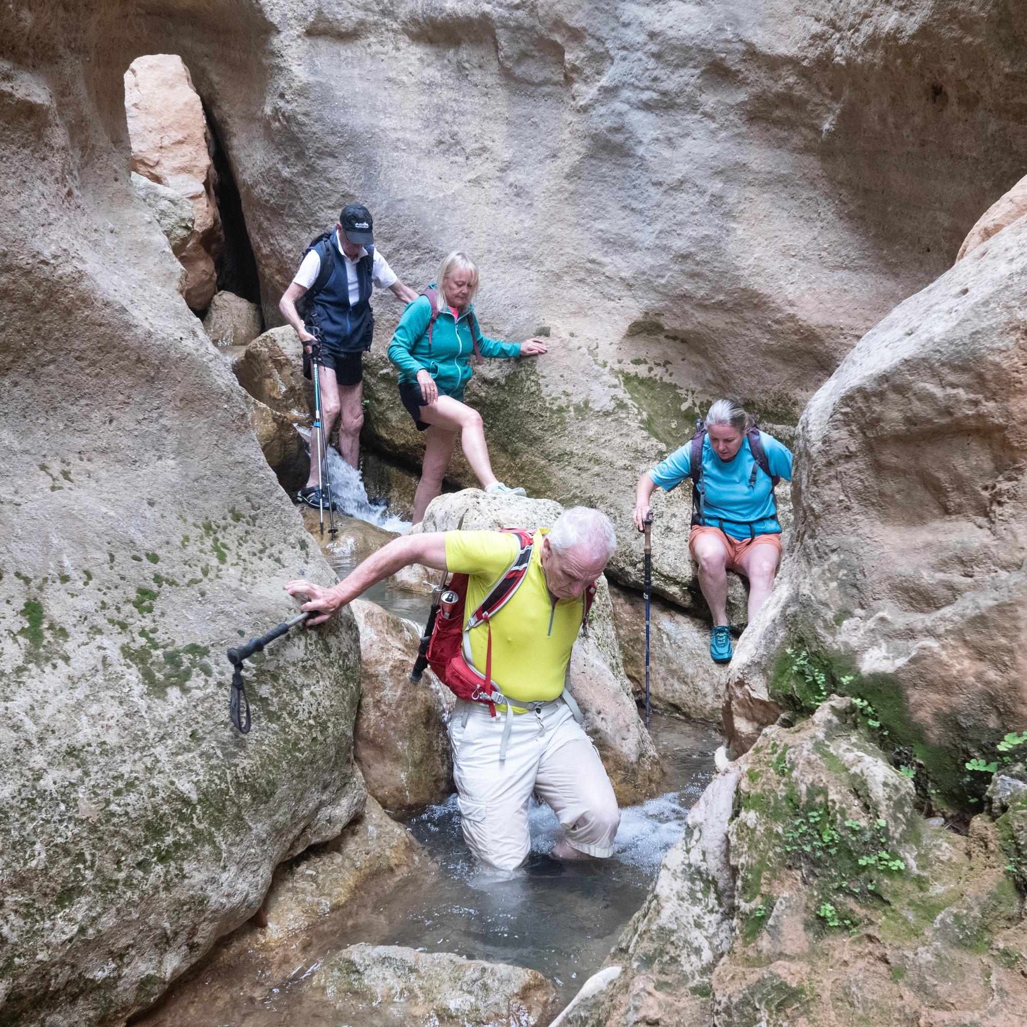 A group of hikers passes down a narrow river gorge with huge rock walls vertically rising above