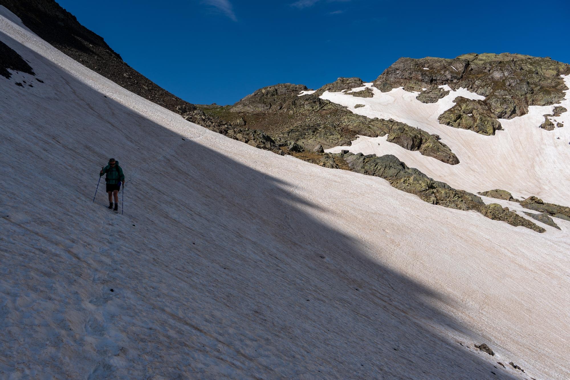A person descends a snow slope in the shade. Behind in a mountain pass between Spain and France, the Puerto de Marcadau 2541m