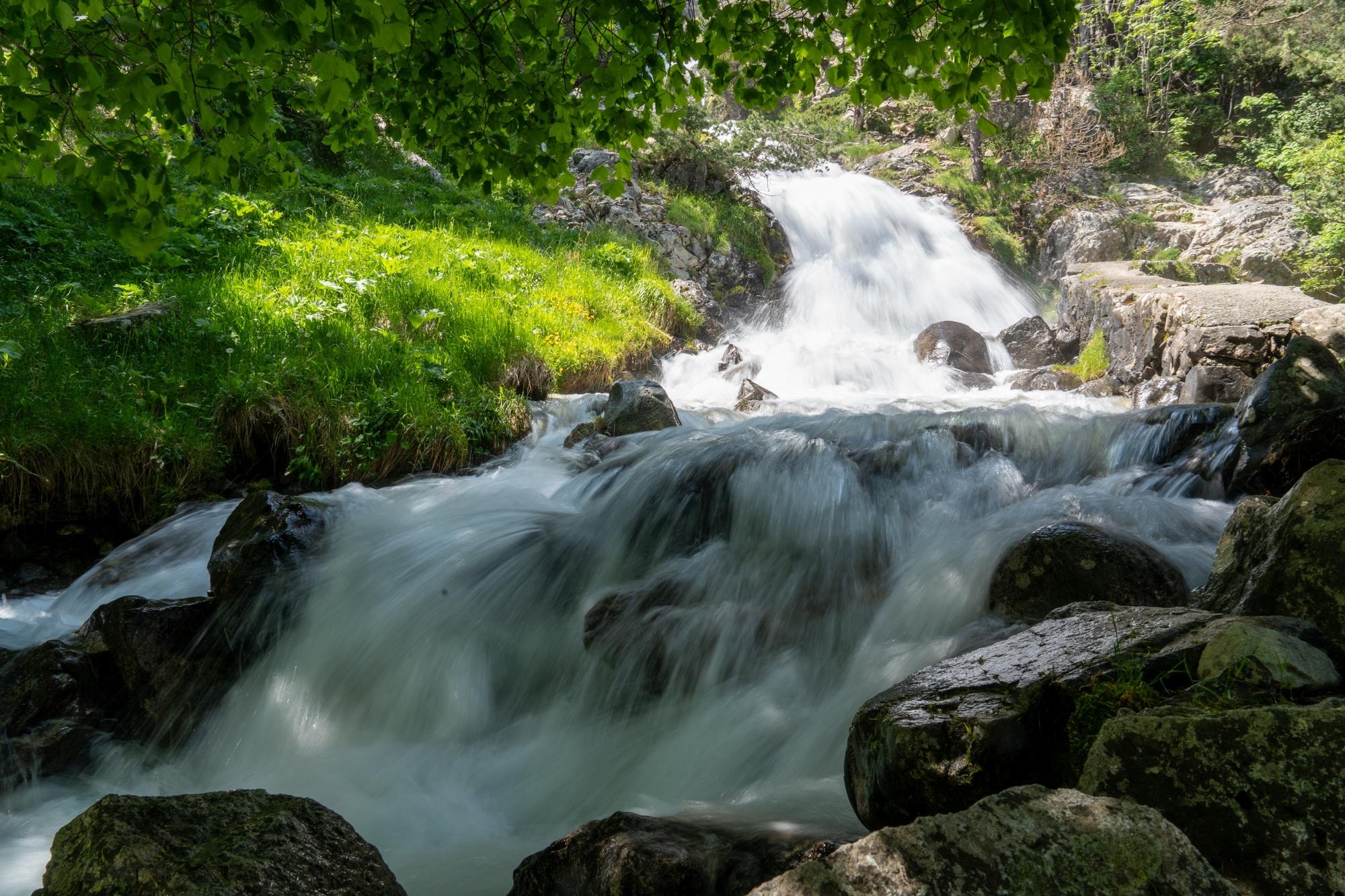 A river drops over a series of spectacular waterfalls. The banks are rich in green vegetation