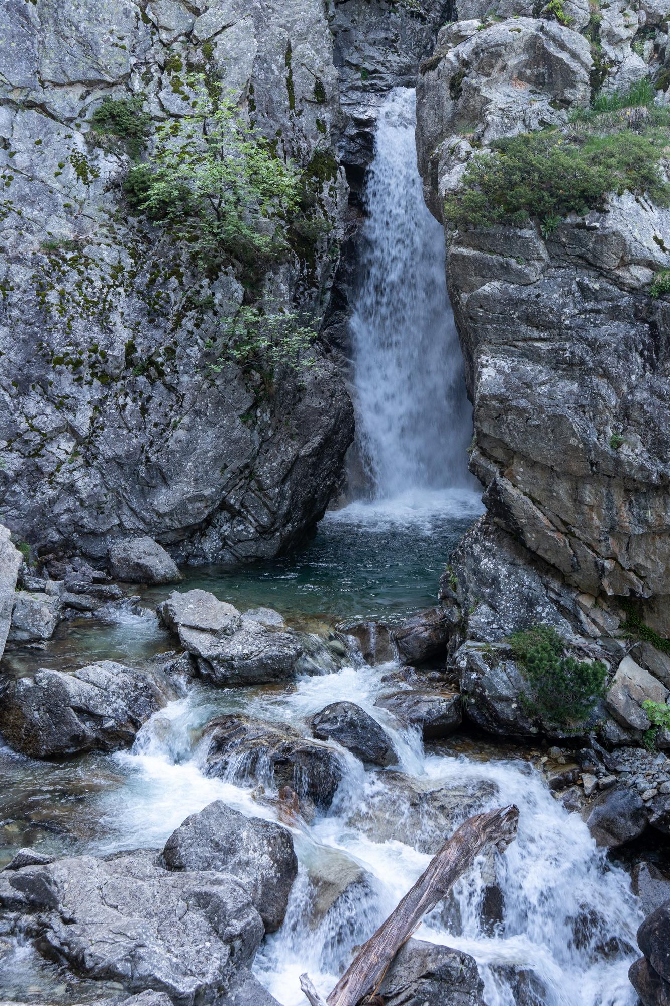 A river drops over a spectacular waterfall between vertical rock walls. and continues downstream over rocks and boulders