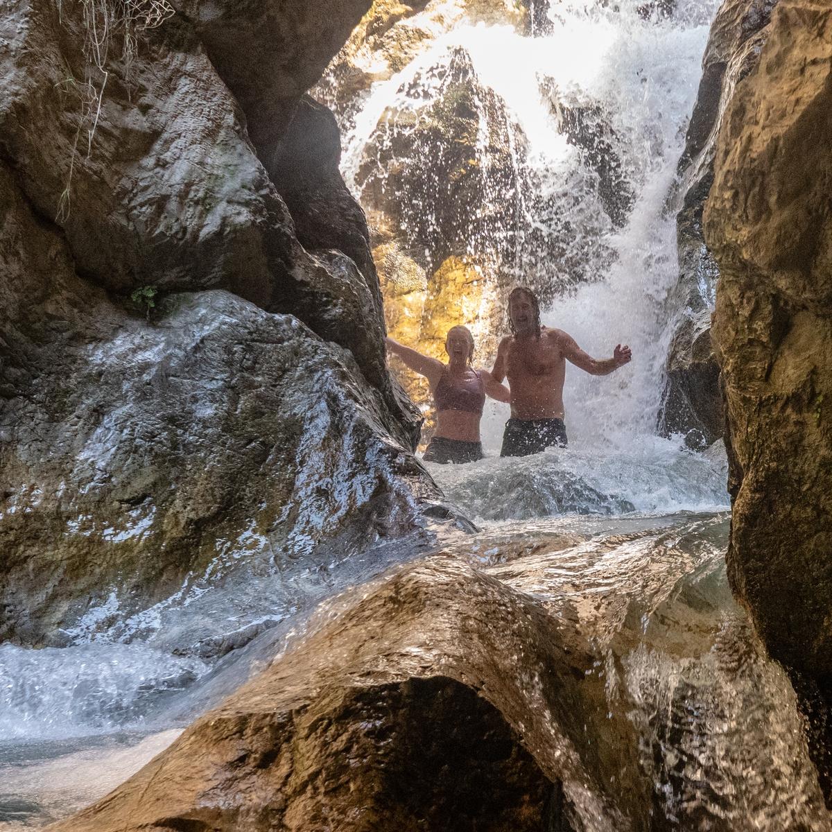 Two people stand under a waterfall