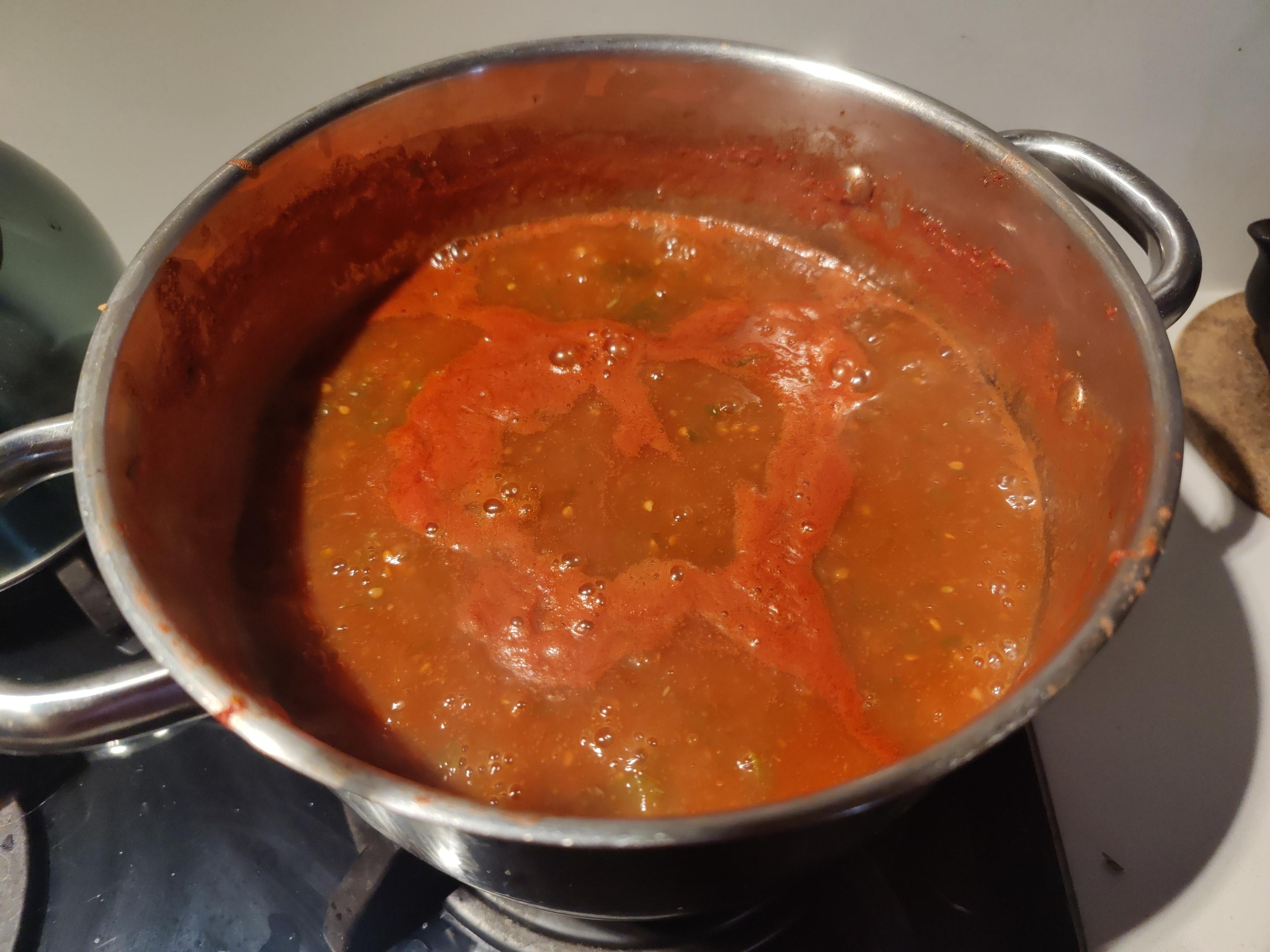 Vibrant red colours from tomatoes booking in a metal pan on a hob