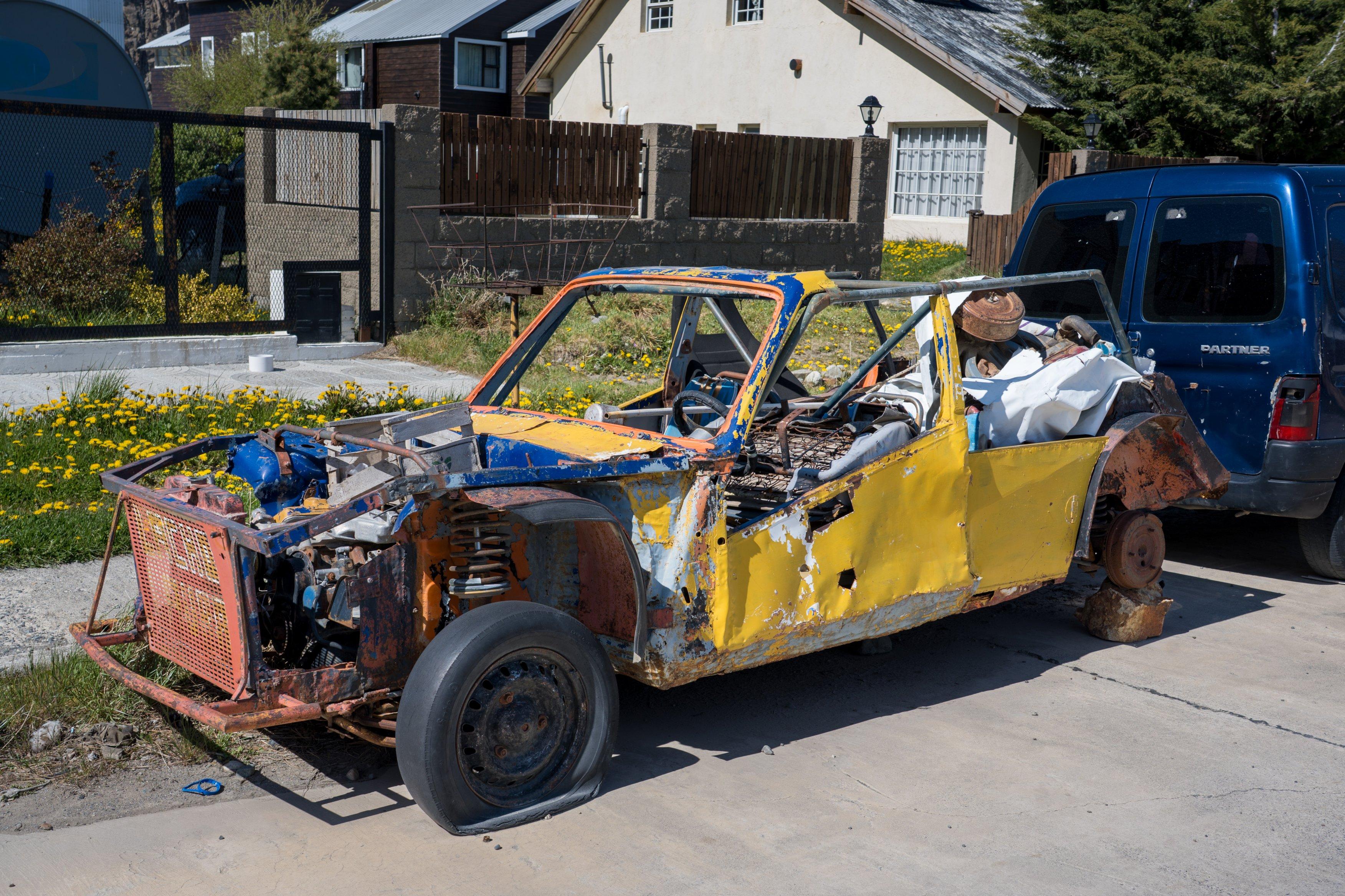 A battered and beat up old yellow car with some blue parts
