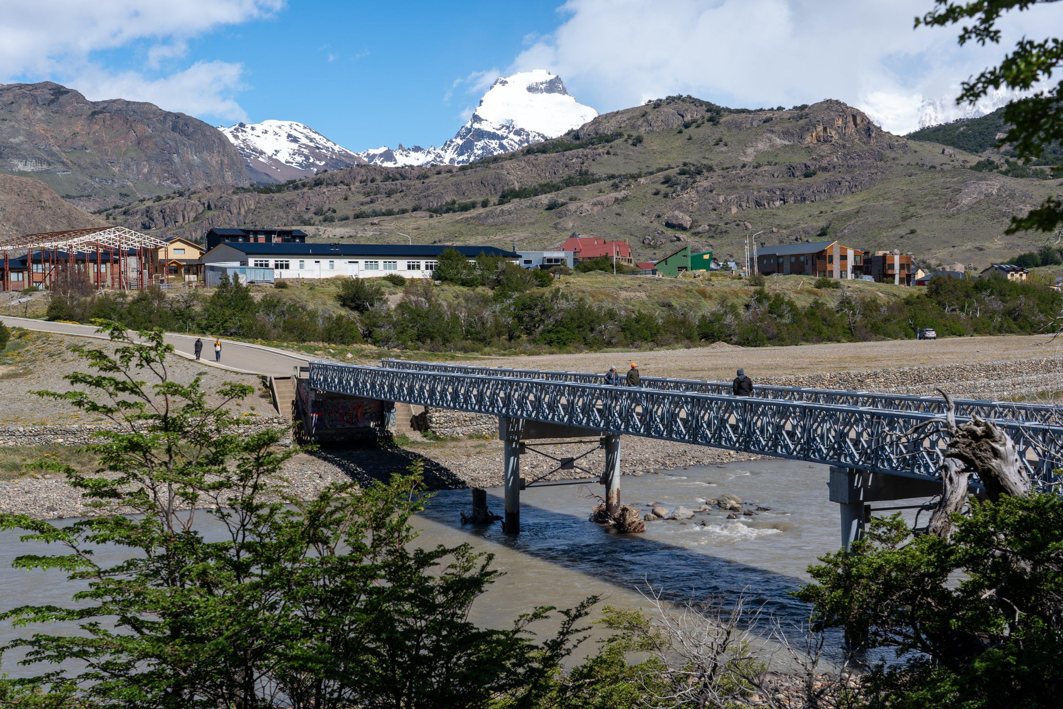 A bridge over the Rio de las Vueltas. Outskirts of El Chalten beyond. Peak is Cerro Solo