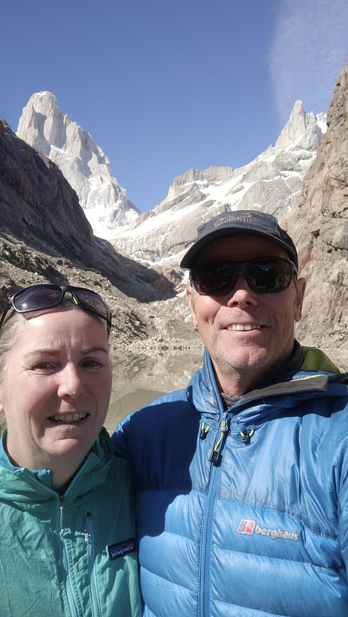 Richard and his wife Kiersten in mountain jackets stand in front of two big mountains in Patagonia. Mt FitzRoy and Cerro Pollone