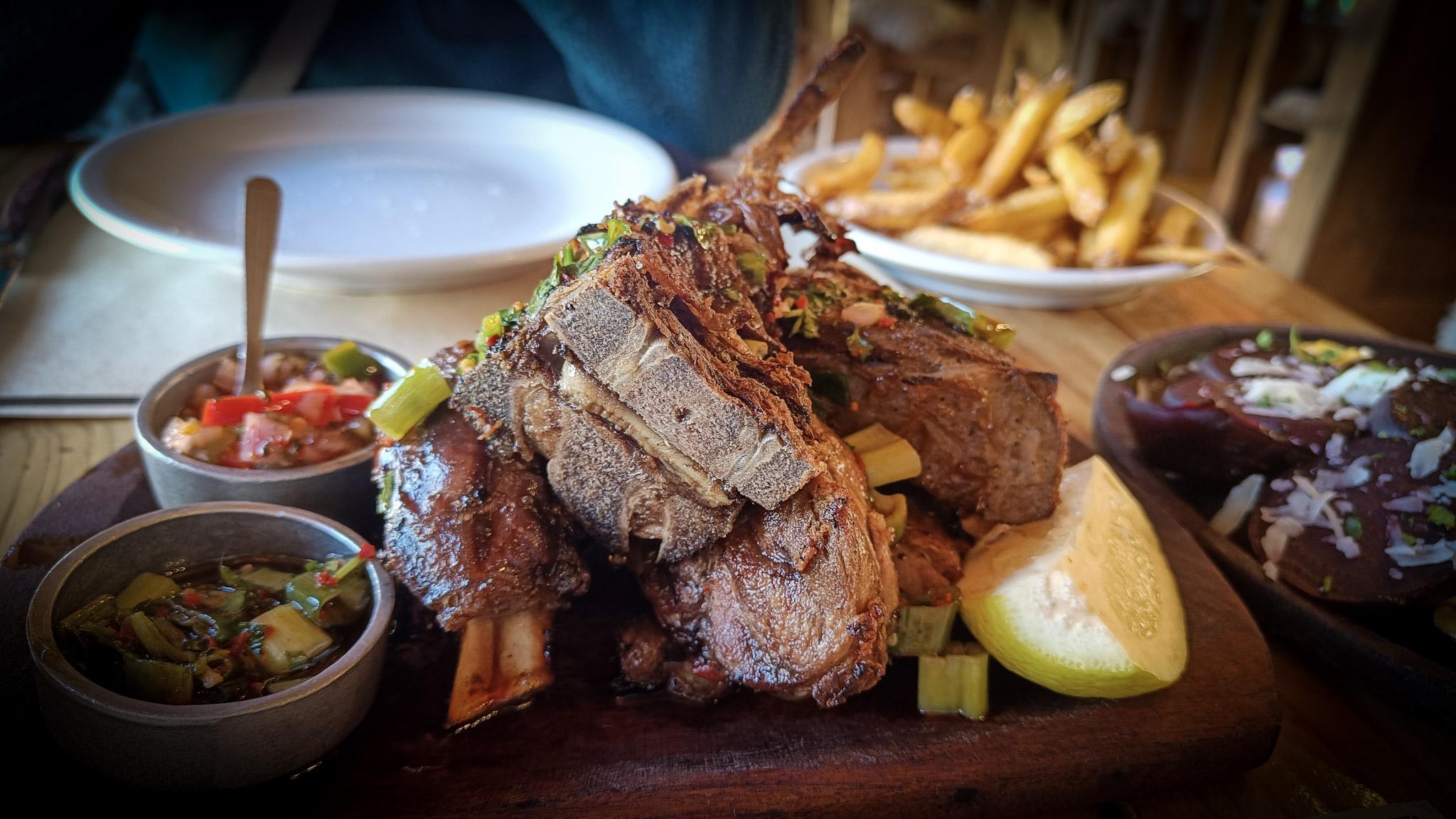 A plate of Patagonian lamb with sime fries behind and some salsa dishes to one side