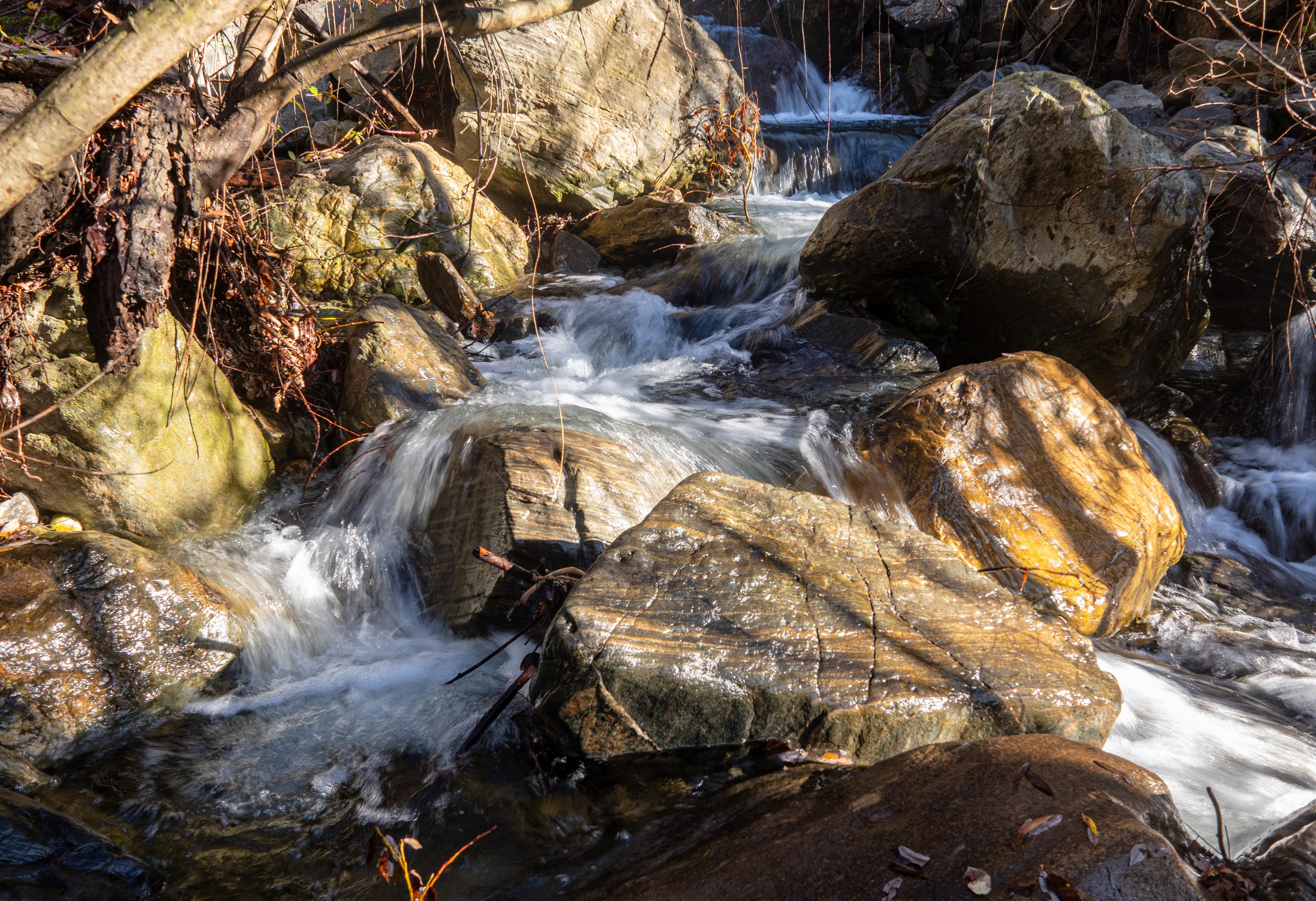 Water coming down a river is blocked by large colourful boulders in the river bed.