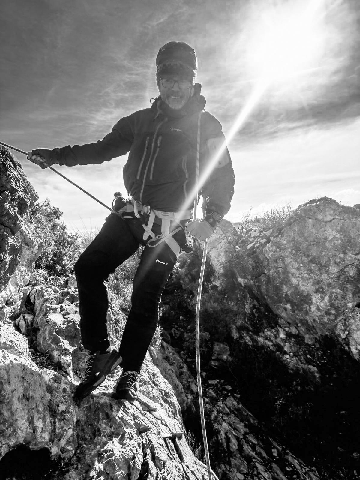 A black and white photo of a climber abseiling down a rope using the Dulfersitz method