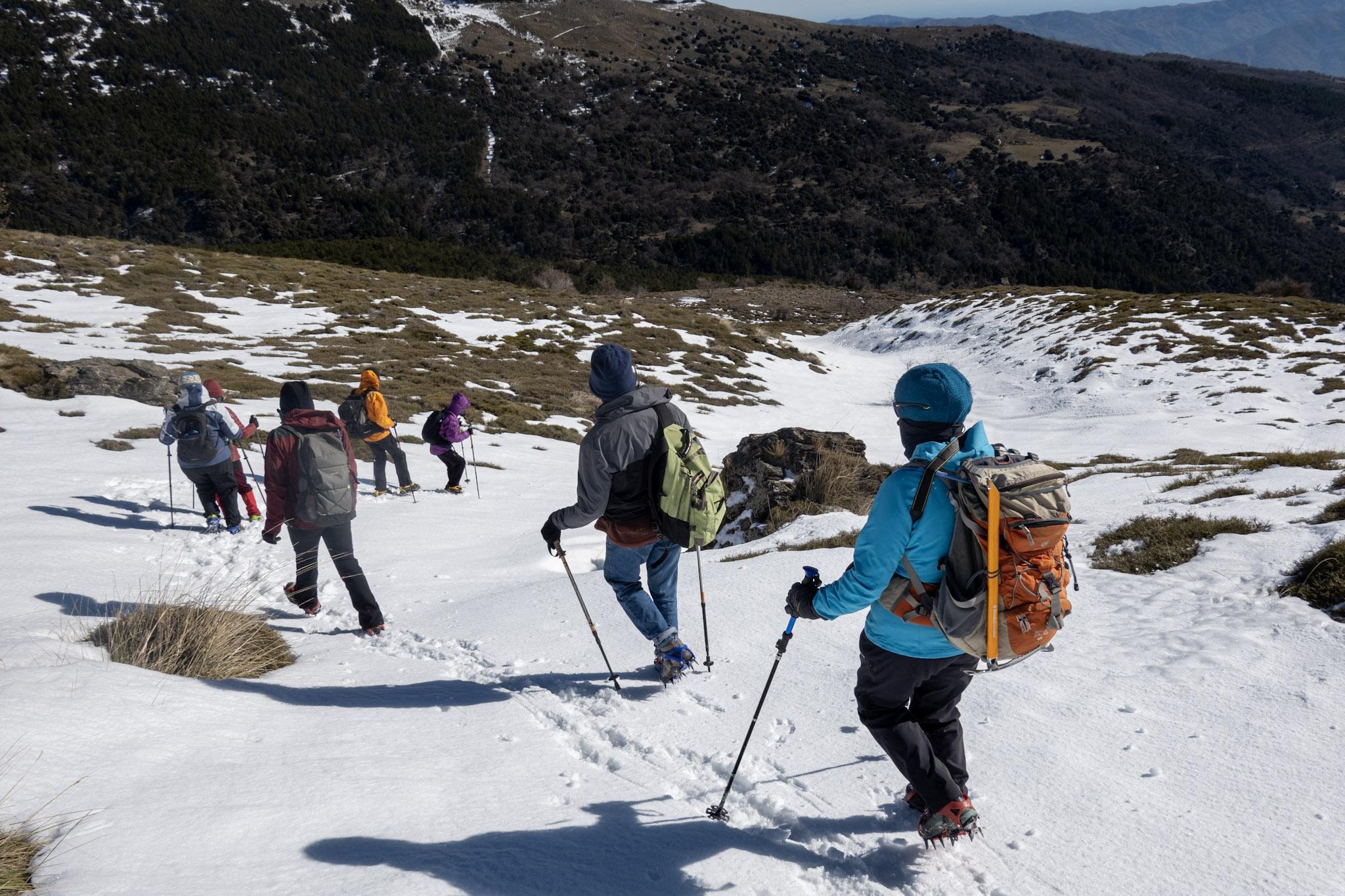 A group of hikers drop down a shallow snow gully towards the base of the mountain