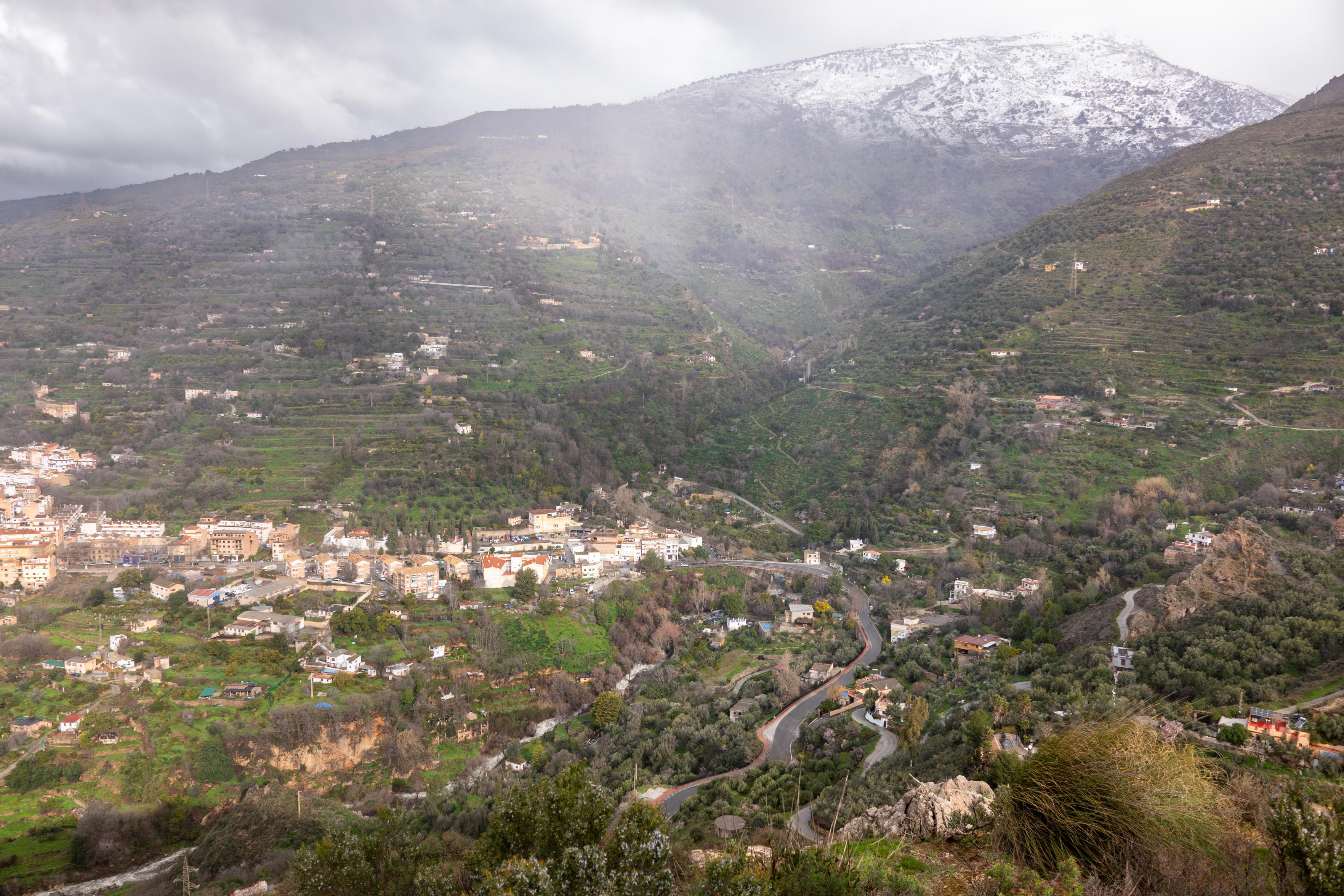 A town nestles below a river valley and high hill with fresh snow on it