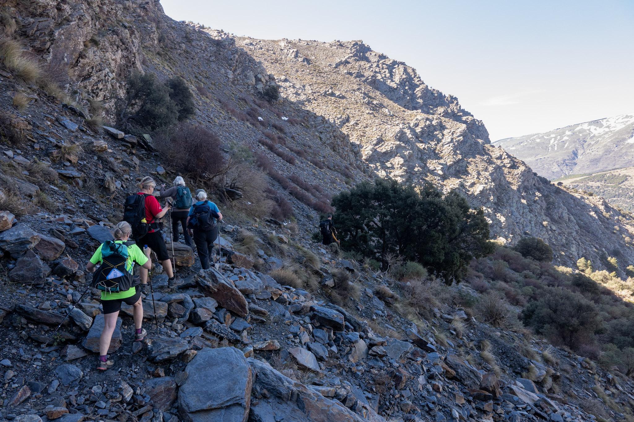 Some hikers pass along a rough mountain track. Ahead lies the summit of Peñabon, the objective