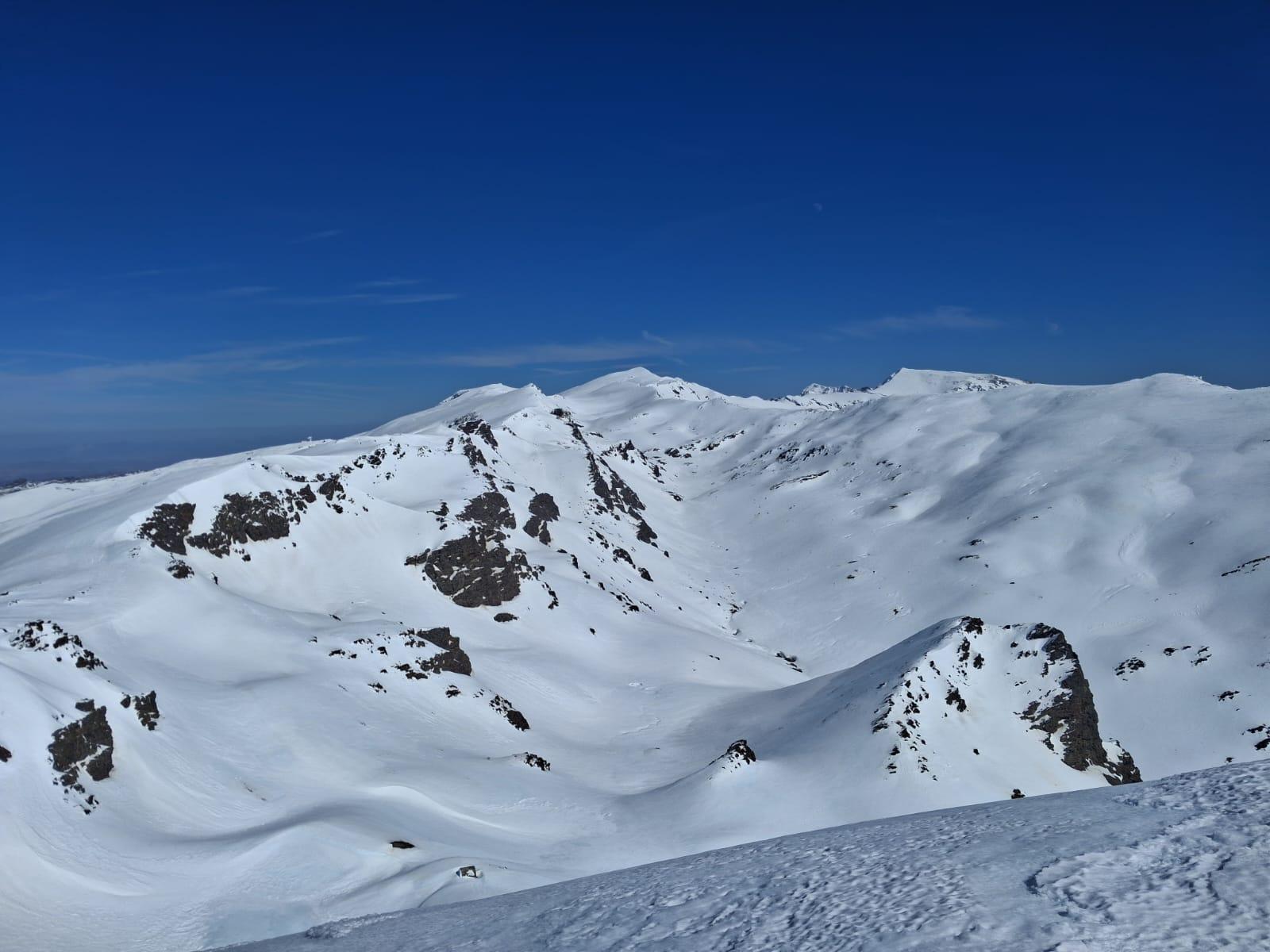 A white mountain world with a deep valley of snow and ice contrasts with blue, cloudless sky above