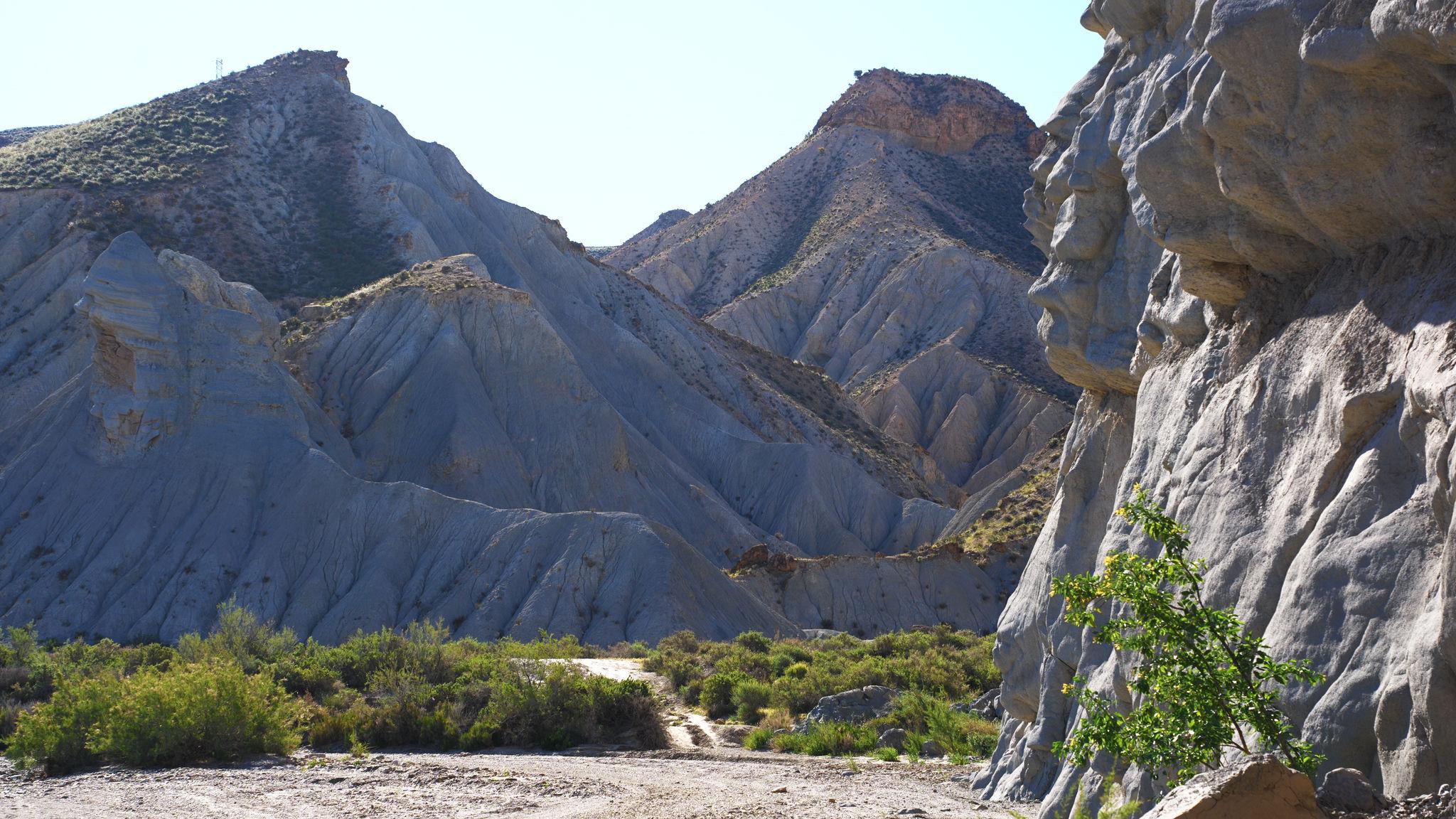 Arid mountain scenery in shadow with a sunlit vertical rock face to the right