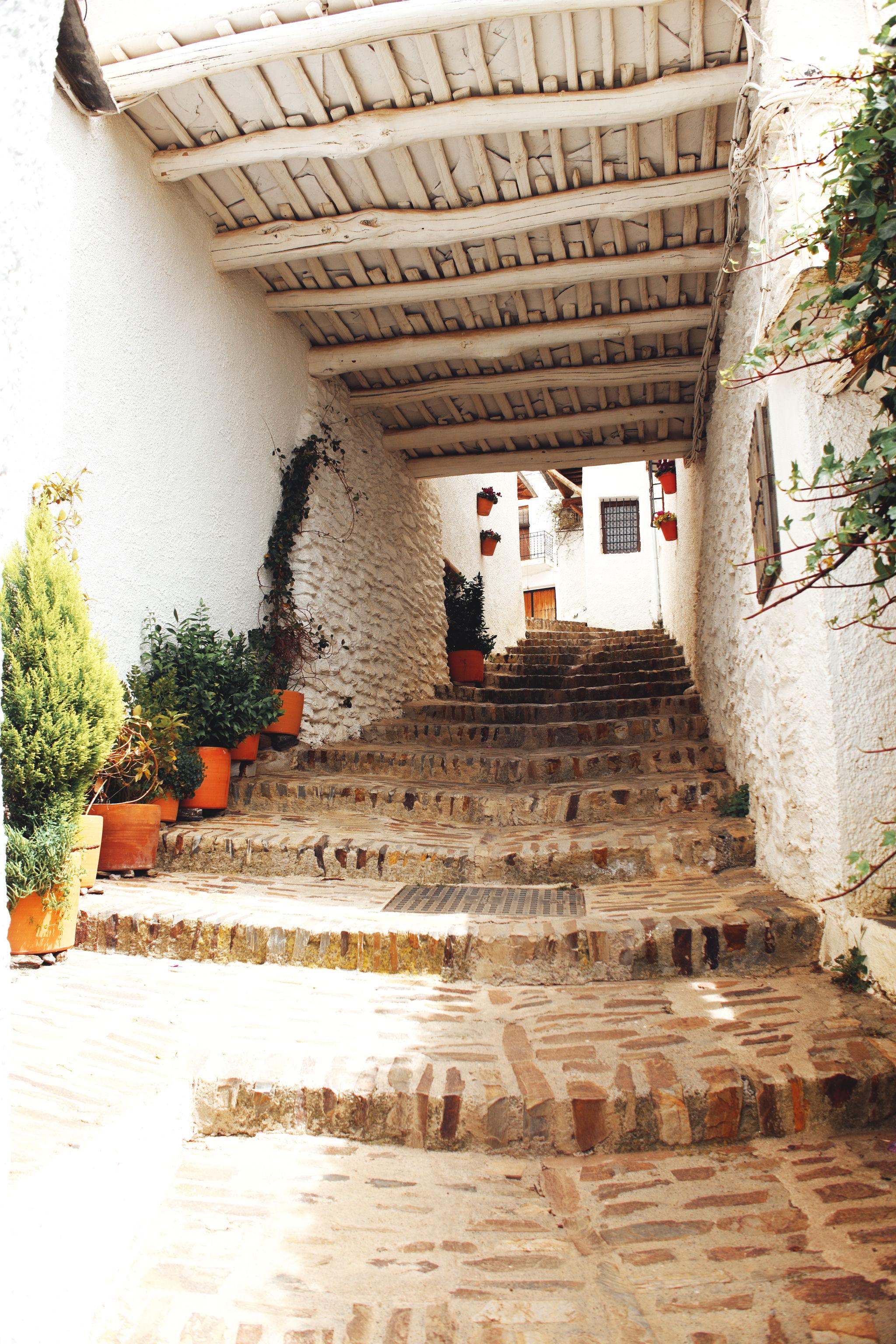 A view up a narrow covered rising, street. The street is covered by a roof built traditionally out of locally found building materials