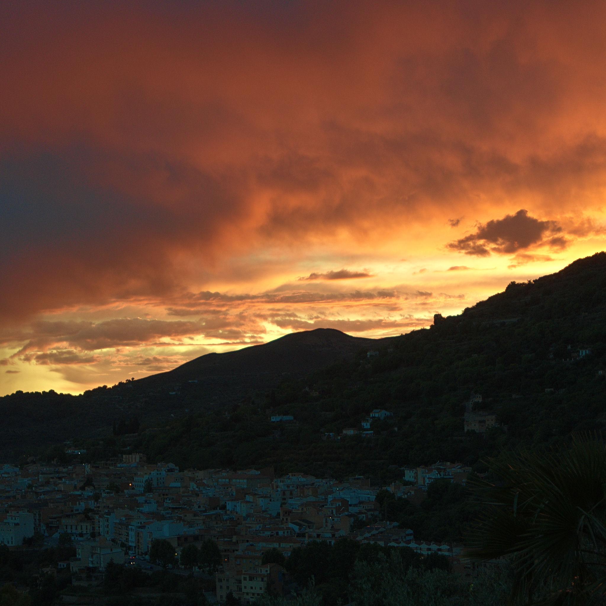 A fiery orange sky above a darkened spanish town at dusk